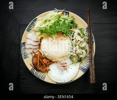 Ein Teller Reis serviert mit Hühnerscheiben, Spiegelei, Garnelen und frischem Gemüse. Stockfoto