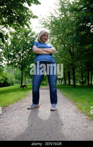 Frau in lässigem Outfit steht selbstbewusst auf einem Weg in einem üppig grünen Park. Stockfoto