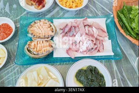 Blick von oben auf authentische koreanische Meeresfrüchte mit frischem Meeräschen-Sashimi, rohen Abalone in Muscheln und Gamtae-Algen-Beilagen in einem traditionellen Restaurant Stockfoto