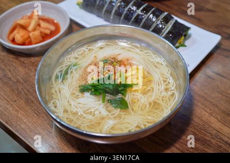 Traditionelle koreanische warme Nudelsuppe, ein in Scheiben geschnittenes Meeresalgen-Reisbrötchen und scharfe gemischte Nudeln mit frischem Gemüse, serviert in authentischen Schüsseln aus rostfreiem Edelstahl. Stockfoto