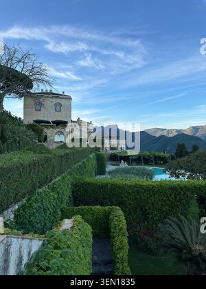 Gepflegte Hecken formen ein grünes geometrisches Labyrinth um eine historische Villa, eingerahmt von Bergen und einem leuchtend blauen Himmel Stockfoto