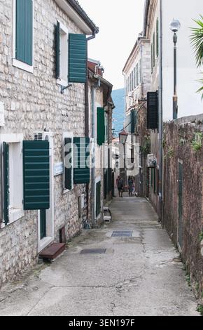 Eine charmante, enge Straße in der historischen Altstadt von Herceg Novi, Montenegro, mit traditionellen Steinhäusern mit grünen Fensterläden. Stockfoto