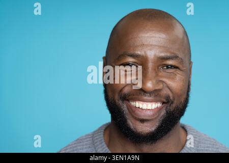 Afroamerikaner mittleren Alters lächelt und posiert im Studio mit blauem Hintergrund in grauem Pullover Stockfoto