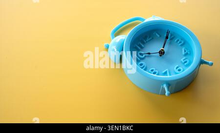Abgewinkelter Schuss eines blauen Weckers mit zwei Glocken auf einer glatten gelben Oberfläche, auf der rechten Seite mit viel Kopierraum. Stockfoto