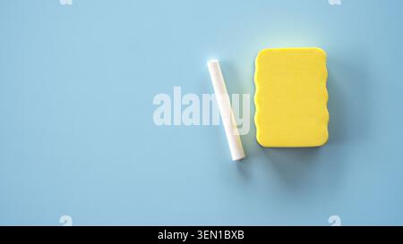 Ansicht von oben nach unten eines weißen Kreidestäbchens und eines gelben Schaumschwammes auf einer durchgehenden hellblauen Oberfläche. Stockfoto