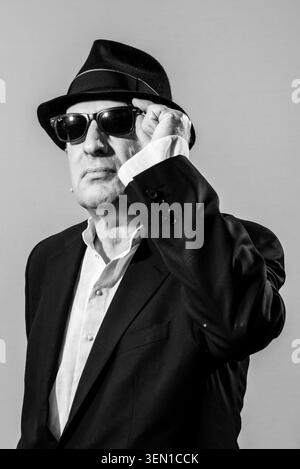 Martin Rowson steht selbstbewusst, während er einen schwarzen Anzug und eine dunkle Sonnenbrille trägt. Er passt seine Brille mit einem ernsten Ausdruck an Stockfoto