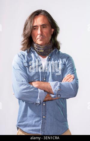 Neil Oliver steht mit überkreuzten Armen, trägt ein Jeansshirt und einen Schal. Die Einstellung ist einfach, mit einem einfachen Hintergrund. Er wirkt nachdenklich und Stockfoto