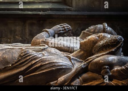 Detaillierte Seitenprofilansicht eines mittelalterlichen Steinfiguren-Grabdenkmals, das eine liegende Figur mit Händen zeigt, die im Gebet in der Tideswell-Kirche eingeschlossen sind Stockfoto