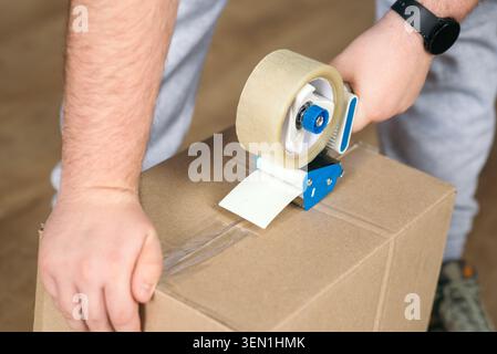 Man versiegelt Pappkarton mit Klebepistolenspender beim Transport oder Verpacken. Stockfoto