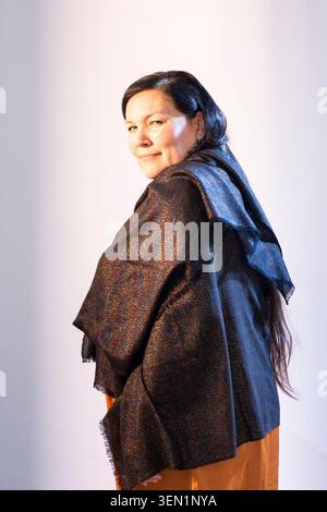 Taqralik Partridge posiert in einem Studio mit hellem Hintergrund. Sie trägt einen Schal und lächelt in die Kamera. Lange Haare fallen ihr auf den Rücken, während sie steht Stockfoto