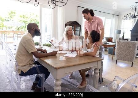 Verschiedene Familien treffen sich am hölzernen Esstisch und lesen Papierkram mit Klemmbrett und Tassen Stockfoto