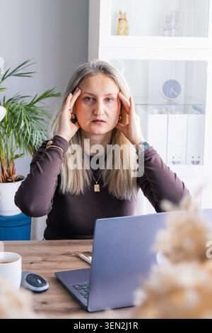 Müde Geschäftsfrau leidet unter Stress und Kopfschmerzen während der Arbeit am Laptop im Heimbüro. Konzept von Burnout, Überlastung, Müdigkeit, geistige Gesundheit, Stockfoto