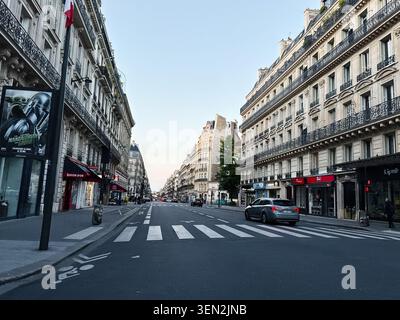Paris, Frankreich - 14. Mai 2026: Ruhige Pariser Avenue bei Sonnenaufgang gesäumt von Haussmann-Architektur, Straßenübergang, Geschäften und leichtem Verkehr. Stockfoto