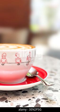 Cappuccino in weißer Tasse mit roter Untertasse auf Kaffeetisch, für städtische Kaffeekultur, Kaffeepause, Fika Visuals, entspannte morgendliche Atmosphäre, soziale Medien Stockfoto