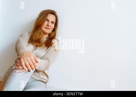 Portrait einer blonden Frau mittleren Alters, die auf dem Boden sitzt Stockfoto