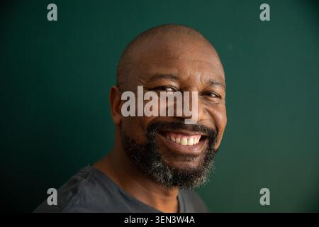 Reifer Afroamerikaner lächelt im Studio vor dunkelgrünem Hintergrund und trägt ein graues T-Shirt Stockfoto