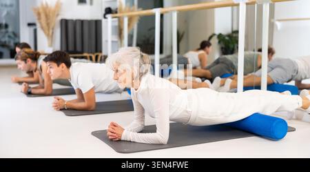 Frauen und Männer, die Yoga-Positionen während des Gruppentrainings im Fitnesscenter ausüben, und Stretching Asana Urdhva Mukha Shvanasana Stockfoto