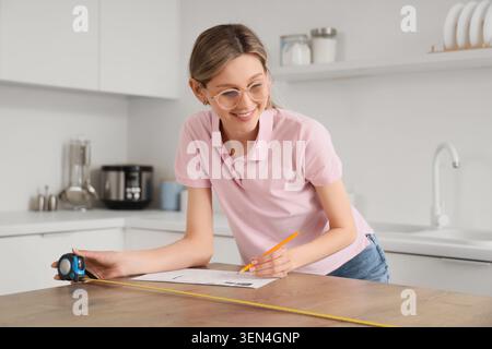 Junge Frau, die Küchenarbeitsplatten für Renovierungsprojekte misst, Innenarchitektur und DIY-Verbesserungen plant, eine junge Frau misst einen Kitc Stockfoto