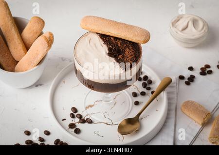 Tiramisu-Dessert im Glas mit Ladyfinger-Keks, Kaffeebohnen und Kakaopulver auf weißem Hintergrund Stockfoto