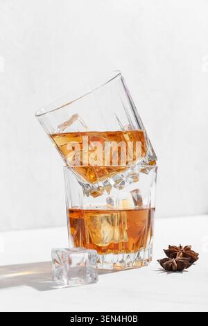 Gestapelte Whiskey-Gläser mit Eiswürfeln und Sternanis, bernsteinfarbenes alkoholisches Getränk, weißer Hintergrund, Getränkeindustrie Stockfoto