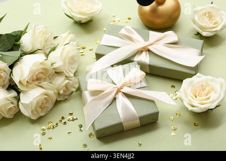 Komposition mit Geschenkboxen, weißen Rosenblüten und einer Flasche Parfüm auf grünem Hintergrund Stockfoto