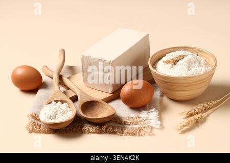 Backzutaten Stillleben mit frischem Hefeblock, Mehl, Eiern und Weizenohren auf beigem Hintergrund Stockfoto