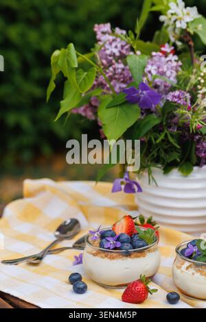 Close Up Käsekuchen Desserttassen mit frischen Beeren und essbaren Blumen Stockfoto