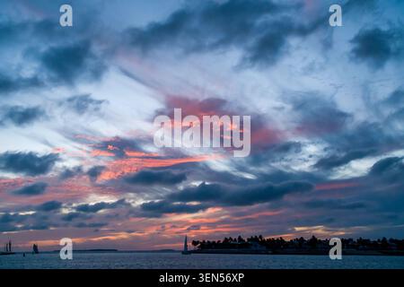 Das kleine Passagiersegelboot überquert den Ozean in der Nähe der dunklen Silhouette von Key West unter einem farbenfrohen Sonnenuntergangshimmel im Sommer. Stockfoto
