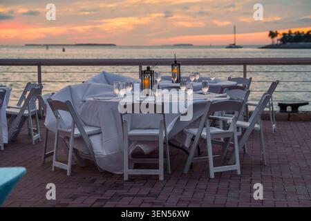 Die runden Banketttische mit den weißen Tischdecken und leeren Stühlen stehen auf dem hölzernen Key West Pier in der Nähe des klaren Meerwassers für die Veranstaltung. Stockfoto