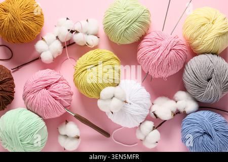 Bunte Garnbällchen und Baumwollbälle mit Stricknadeln und Häkelnadel auf rosa Hintergrund, Stricknadeln und Häkelnadel werden unter t platziert Stockfoto