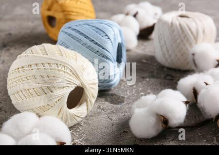 Baumwoll-Kugeln und Baumwoll-Bollenbälle auf strukturiertem grauen Hintergrund für Textil- und Bastelprojekte, diese Komposition unterstreicht die natürliche ori Stockfoto