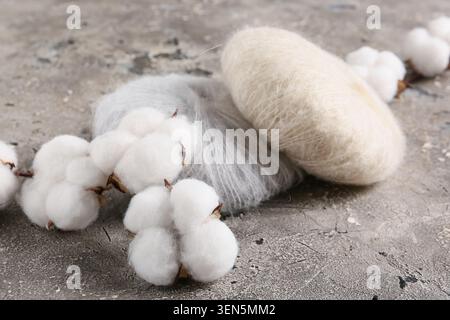 Natürliche Baumwoll-Bollen und weiche Garnstränge auf strukturiertem grauen Hintergrund, Textilhandwerk und organisches Materialkonzept, die weißen Baumwollfasern stehen im Kontrast zu wi Stockfoto