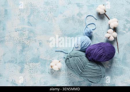 Bunte Garnbällchen und Baumwollbälle auf strukturiertem blauem Hintergrund für Bastel- und Strickprojekte Stockfoto