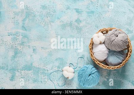Bastel- und Strickbedarf mit Baumwoll-Garnbällchen und natürlichen Baumwoll-Bollen in einem Korb auf blauem Hintergrund, handgefertigt Stockfoto