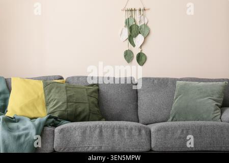 Gemütliches Wohnzimmer mit grauem Sofa, farbenfrohen Kissen und Makramee-Blatt-Wanddekor, Wohnkomfort und modernem Design Stockfoto