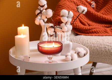 Gemütliches Ambiente mit zündeten Kerzen, Baumwollstielen und warmer Strickdecke auf einem Beistelltisch Stockfoto