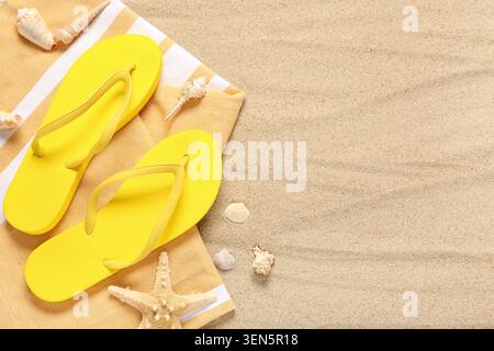 Die Grundausstattung für den Sommerurlaub am Strand mit gelben Flipflops, gestreiftem Handtuch, Seesternen und Muscheln auf Sandgrund Stockfoto