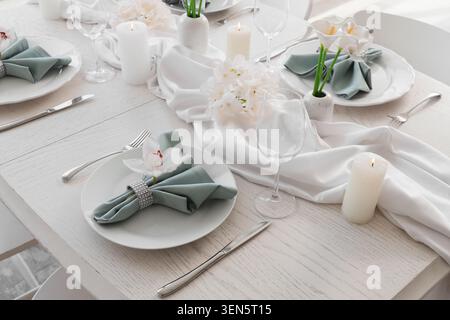 Eleganter Tisch für den Hochzeitsempfang mit weißen Tellern, grünen Servietten, Besteck und Blumendekorationen Stockfoto