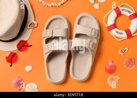 Die wichtigsten Reiseutensilien für den Sommer mit Sandalen, Strohhut, Sonnenbrille und Muscheln auf orangefarbenem Hintergrund Stockfoto
