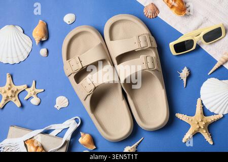 Grundausstattung für Sommerurlaub am Strand mit beigen Sandalen, Sonnenbrillen, Muscheln und Seesternen auf blauem Hintergrund Stockfoto