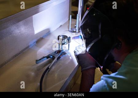 Ein professioneller Schweißer führt Argon-WIG-Schweißen auf Edelstahl durch, wodurch eine präzise und saubere Schweißnaht unter kontrollierten industriellen Bedingungen erzeugt wird. Th Stockfoto