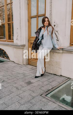 Frau Mode urbane junge Frau mit blauem Hemd und Jeans, die sich an ein klassisches Steingebäude in der Stadt lehnt Stockfoto