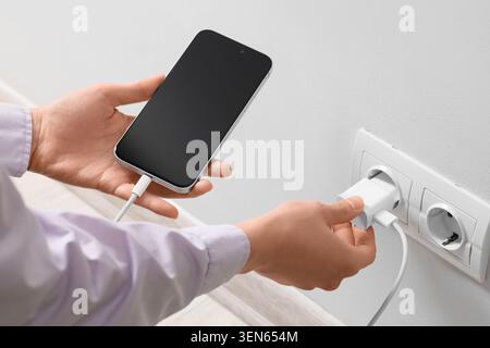 Person, die ein weißes USB-C-Ladegerät in eine Steckdose einsteckt, um ein modernes Smartphone mit leerem Bildschirm aufzuladen Stockfoto
