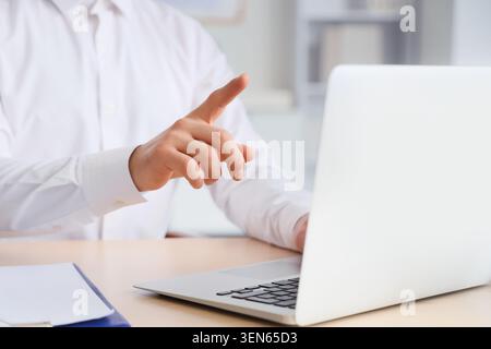Geschäftsmann, der während einer Online-Präsentation oder eines virtuellen Meetings in einer modernen Büroumgebung auf den Laptop-Bildschirm zeigt, Stockfoto