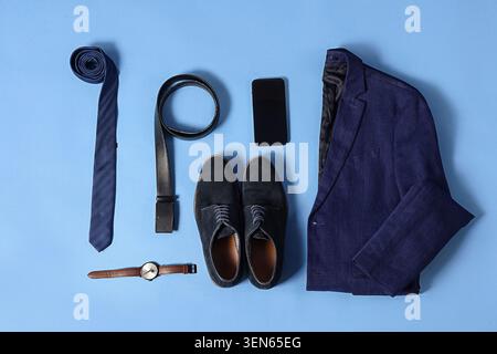 Professionelle Herren Business Kleidung flach gelegt mit marineblauem Anzug Jacke Krawattengürtel Schuhe Uhr und Smartphone auf blauem Hintergrund Stockfoto