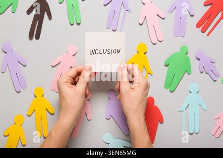 Einbeziehung mit verschiedenen Papierfiguren und Händen, die ein „Inklusion“-Schild auf grauem Hintergrund halten, werden Konzepte für Inklusion und Vielfalt durch dargestellt Stockfoto