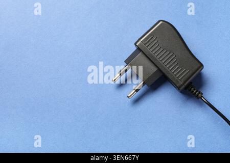 Schwarzes Netzteil mit zweipoligem Stecker und Kabel auf blauem Hintergrund, elektrisches Gerät zum Laden von Elektronik, für das dieses elektrische Gerät verwendet wird Stockfoto