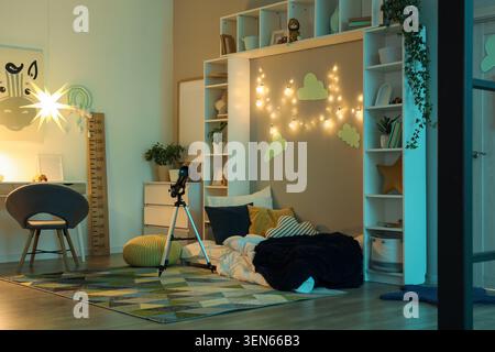Gemütliches Kinderzimmer mit Teleskop, Schreibtisch, Bett und dekorativer Beleuchtung für fantasievolles Spielen und Lernen Stockfoto