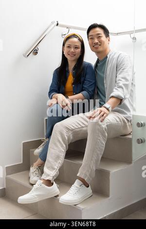 Verschiedene Paare sitzen auf gekachelten Treppen, lächeln, tragen weiße Sneakers und Smartwatch Stockfoto
