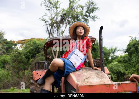 Junge Frau Traktor Strohhut ländliches Feld kariertes Hemd insgesamt Stiefel ländliche Farm Stockfoto